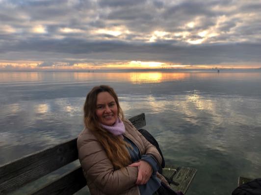 Lene Wiklund på en bænk ved vandet i solnedgang